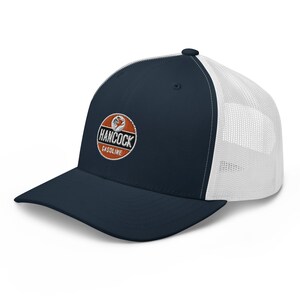 May include: A navy blue and white trucker hat with a vintage-style logo that reads "Hancock Gasoline". The logo is a circle with an orange background and white lettering.