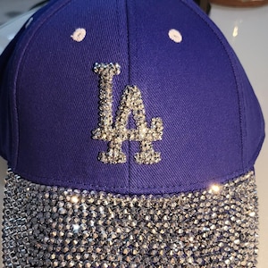 May include: A royal blue baseball cap with a silver rhinestone 'LA' logo and a silver rhinestone brim.