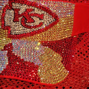 May include: A red sequined fabric with a red, white, and gold rhinestone design of the Kansas City Chiefs logo.