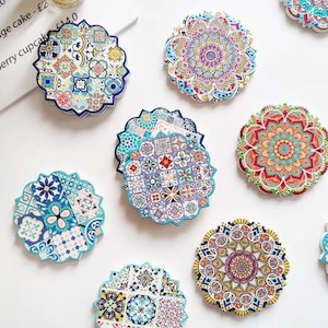 Puede incluir: Colección de posavasos decorativos con diseños intrincados. Los posavasos presentan una variedad de patrones, incluyendo motivos florales y geométricos, en tonos azules, rojos, amarillos y blancos. Cada posavasos tiene un borde festoneado.