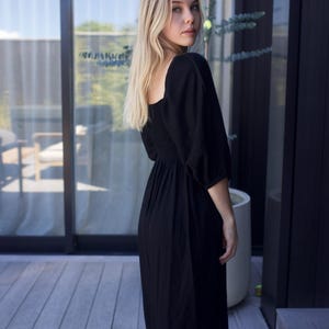 Puede incluir: Una mujer con un vestido midi negro de cuello cuadrado y mangas abullonadas. El vestido tiene un corpi&ntilde;o ajustado y una falda fluida.