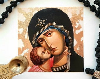 May include: A religious icon depicting the Virgin Mary holding a baby Jesus. The icon is painted in a traditional style with a gold background and the figures are depicted in a realistic manner. The Virgin Mary is wearing a blue and black robe and has a halo around her head. The baby Jesus is wearing a white robe and is looking up at the Virgin Mary.
