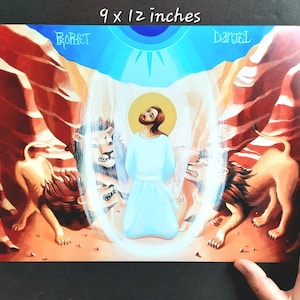 May include: A print depicting a biblical scene, measuring 9 x 12 inches. The artwork features a central figure in a light blue robe, surrounded by lions and bathed in a radiant light. The words "Prophet" and "Daniel" are visible.