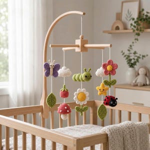May include: A wooden nursery mobile featuring crocheted figures suspended from a central frame. The hanging elements include a purple butterfly, a green caterpillar, a pink flower, a ladybug, a yellow star, white clouds, and red mushrooms.