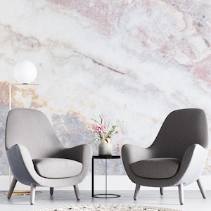 Peut inclure: Deux fauteuils gris rembourr&eacute;s avec dossiers incurv&eacute;s et pieds en bois, une petite table d'appoint ronde noire avec un vase en c&eacute;ramique contenant des fleurs roses, un lampadaire globe blanc et un tapis rond tiss&eacute; blanc sur un mur en marbre.