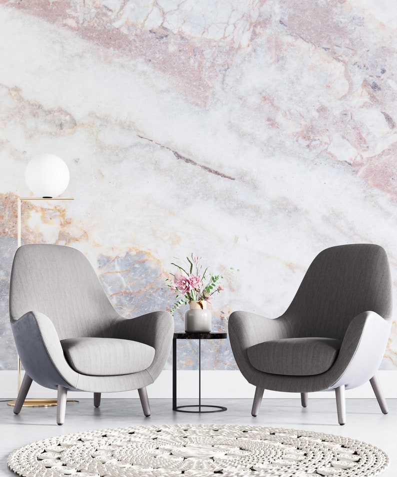Peut inclure: Deux fauteuils gris rembourr&eacute;s avec dossiers incurv&eacute;s et pieds en bois, une petite table d'appoint ronde noire avec un vase en c&eacute;ramique contenant des fleurs roses, un lampadaire globe blanc et un tapis rond tiss&eacute; blanc sur un mur en marbre.
