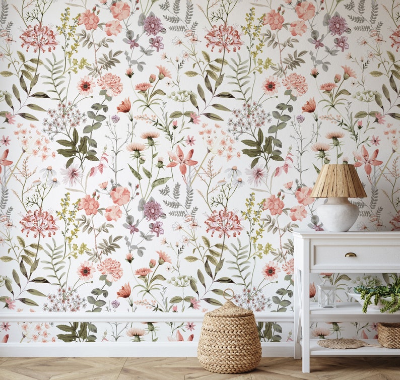 May include: A white wall with a floral wallpaper featuring a variety of pink and green flowers. A white nightstand with a wicker lampshade and a woven basket are in the foreground.