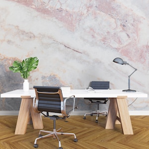 Peut inclure: Un bureau rectangulaire blanc avec des pieds en bois clair, deux chaises de bureau noires, un vase blanc avec des feuilles de monstera vertes, une pile de livres et une lampe de bureau noire devant un mur au motif marbre rose, blanc et gris.