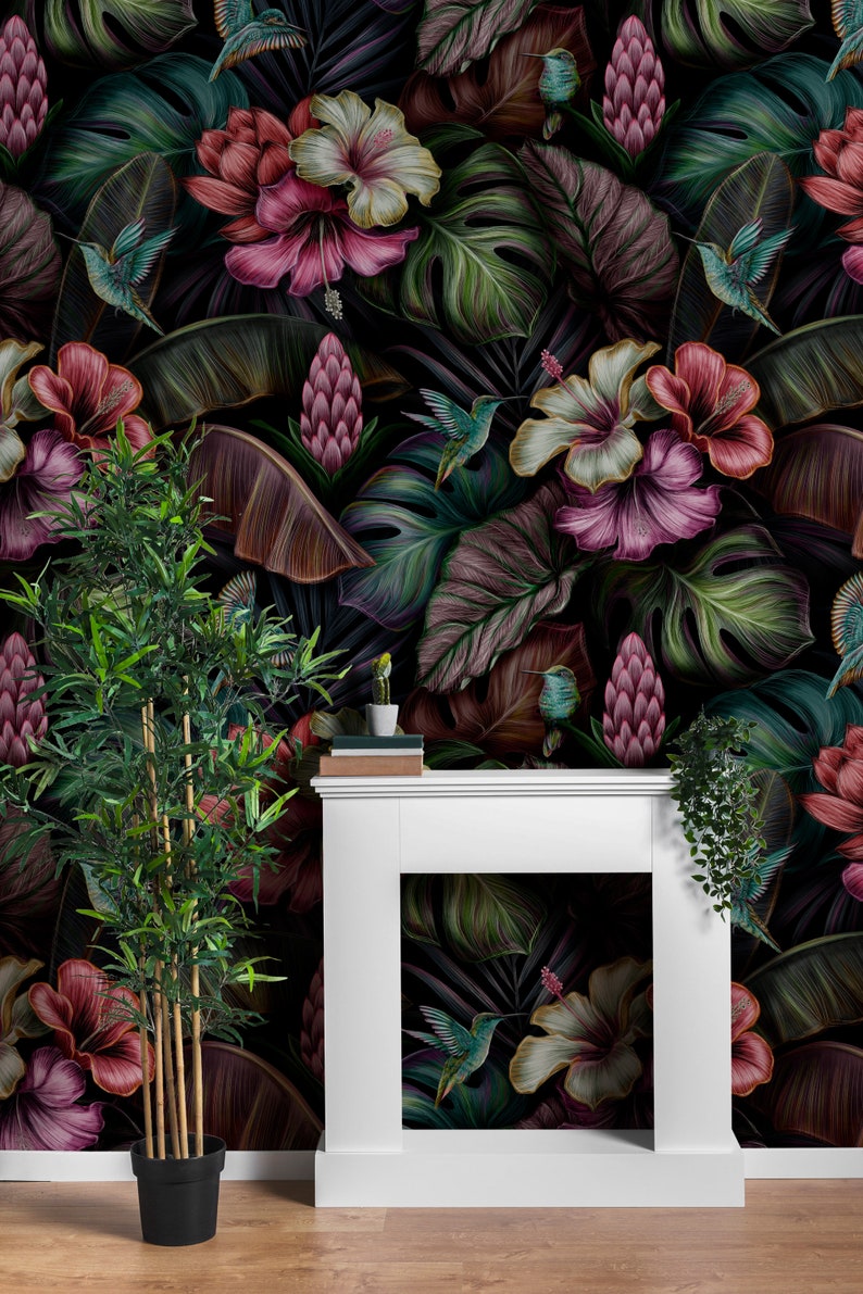 May include: A white fireplace mantel stands against a wall covered in dark wallpaper featuring a tropical pattern of pink and white hibiscus flowers, large green and purple leaves, and small hummingbirds in flight with a potted bamboo plant.