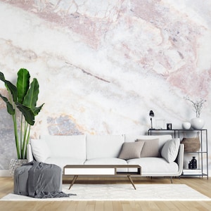 Peut inclure: Un canap&eacute; blanc avec deux coussins gris, une table basse en bois avec un tiroir blanc, un pouf gris avec un tissu drap&eacute;, une grande plante verte dans un pot textur&eacute; et une &eacute;tag&egrave;re en m&eacute;tal noir contre un mur en marbre blanc et rose.
