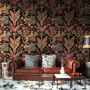 May include: A brown leather sofa with two plush pillows sits in front of wallpaper featuring a repeating pattern of leopards, pink palm leaves, and gold foliage on a black background. A floor lamp with a striped shade stands to the right.
