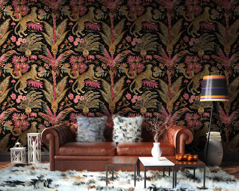 May include: A brown leather sofa with two plush pillows sits in front of wallpaper featuring a repeating pattern of leopards, pink palm leaves, and gold foliage on a black background. A floor lamp with a striped shade stands to the right.