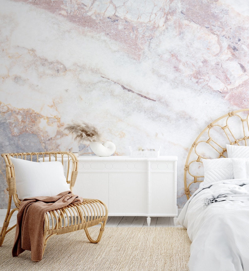 Peut inclure: Une chambre avec un mur au motif de marbre blanc et rose &agrave; grande &eacute;chelle. La pi&egrave;ce comprend une chaise en rotin avec un plaid marron, un buffet blanc et un lit avec une t&ecirc;te de lit en rotin pos&eacute; sur un tapis beige textur&eacute;.