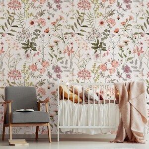 May include: A white crib with a pink and white floral wallpaper background. The crib has a white mattress and a pink blanket. There is a white chair with a black and white checkered pattern in the foreground.