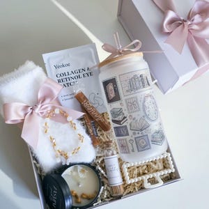 May include: A gift box containing a frosted glass tumbler with a bamboo lid and straw, a pair of white fuzzy socks with a pink ribbon, a Yeokoe collagen and retinol eye patch packet, a candle, a small bottle of matches, and a beaded bracelet.
