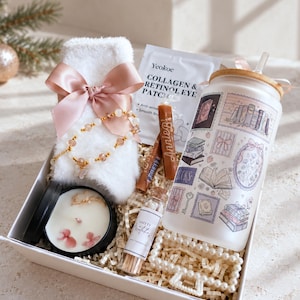 May include: A gift box containing a white fuzzy sock with a pink ribbon, a Yeokoe Collagen & Retinol Eye Patch packet, a frosted glass tumbler with book-themed illustrations, a black candle tin with floral wax, a small bottle of safety matches, and a pearl hair clip.