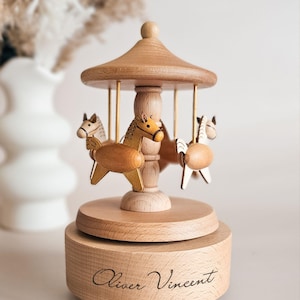 A wooden carousel with horses on it, placed on a wooden base with the name "Olivier Vincent" written on it.