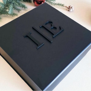 A black gift box with the initials "IB" embossed on it, surrounded by Christmas decorations such as a pine branch and a red ornament.