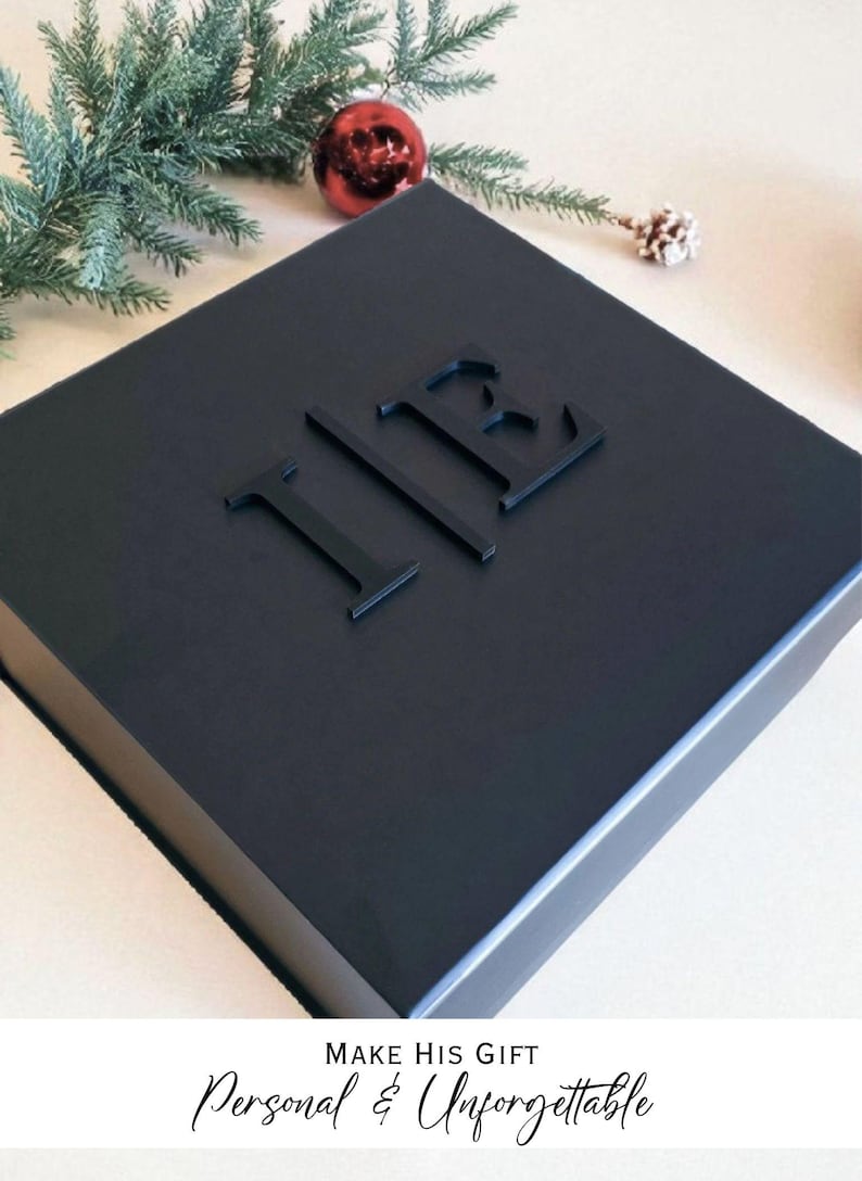 A black gift box with the initials "IB" embossed on it, surrounded by Christmas decorations such as a pine branch and a red ornament.