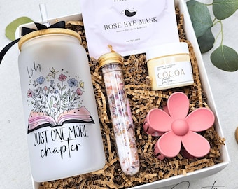 May include: A gift box containing a frosted glass tumbler with a bamboo lid, a clear straw, and the text 'Lily' and 'JUST ONE MORE CHAPTER' with a floral book graphic. Includes a Peauamie rose eye mask, cocoa butter, a floral bath salt tube, and a pink flower hair clip.
