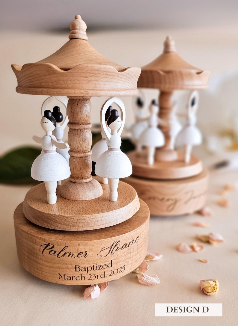 two wooden carousel-like objects with white figures on them, placed on a table with scattered flower petals around them.