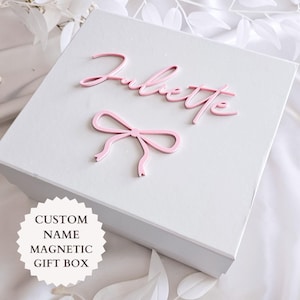 May include: A square white magnetic gift box featuring the name Juliette in raised pink script lettering and a pink bow icon. A white circular badge on the box displays the text CUSTOM NAME MAGNETIC GIFT BOX in black capital letters.