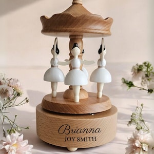 A wooden carousel with three white ballerina figurines on top, surrounded by pink flowers.