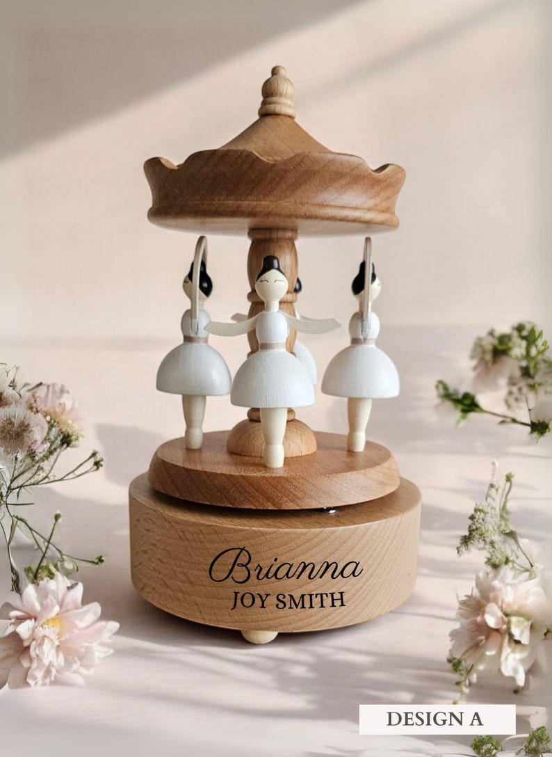 A wooden carousel with three white ballerina figurines on top, surrounded by pink flowers.
