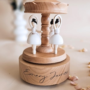 A wooden carousel with three white figurines on top, sitting on a wooden base with the name "Emory James" written on it.