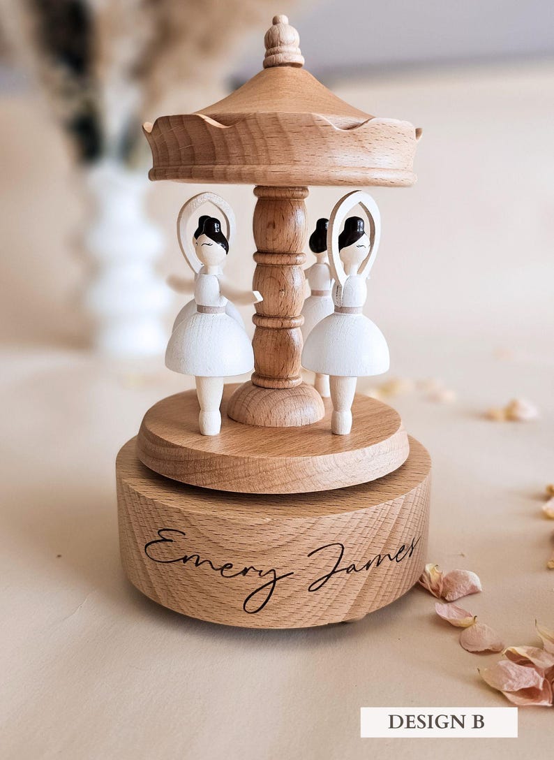 A wooden carousel with three white figurines on top, sitting on a wooden base with the name "Emory James" written on it.