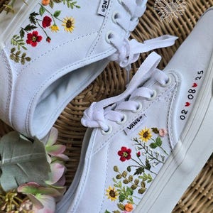 Könnte beinhalten: Weiße Vans-Sneaker mit farbenfrohen Blumenstickereien. Die Stickerei umfasst rote, gelbe und rosa Blumen, mit den Initialen "MVF" und dem Datum "02 08 25" in rotem Faden gestickt.