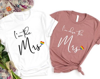 May include: Two white t-shirts with the text "I'm the Mrs" and "I'm also the Mrs" in black script. Each shirt has a rainbow heart.