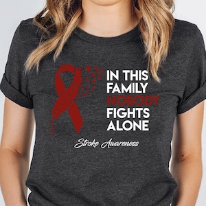 May include: Heather dark grey t-shirt with a red ribbon and the text "In this family nobody fights alone. Stroke Awareness."