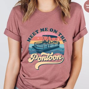 May include: Mauve t-shirt with a retro design. The graphic shows a pontoon boat on water with a sunset background and the text "Meet Me On The Pontoon" in a vintage font.