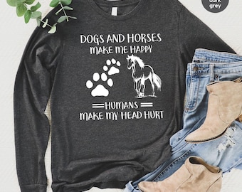 May include: A heather dark grey long-sleeve shirt featuring white text that reads DOGS AND HORSES MAKE ME HAPPY HUMANS MAKE MY HEAD HURT, accompanied by a white graphic of a dog paw print and a horse silhouette, paired with blue denim jeans.