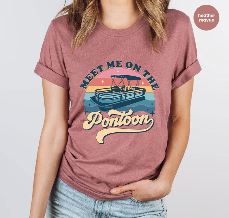 May include: Mauve t-shirt with a retro design. The graphic shows a pontoon boat on water with a sunset background and the text "Meet Me On The Pontoon" in a vintage font.