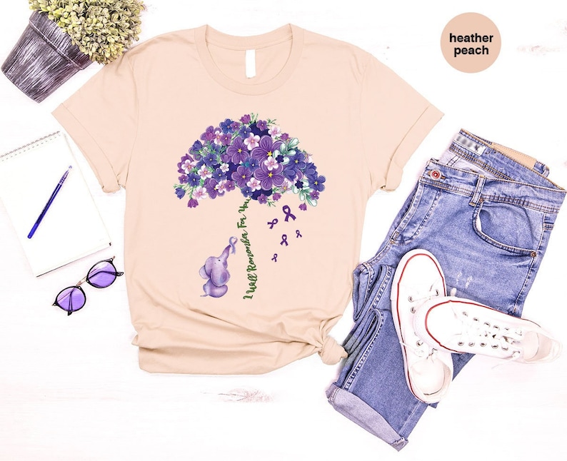 May include: A heather peach t-shirt with a purple flower bouquet and a small elephant holding a purple ribbon. The text "I Will Remember For You" is written on the shirt.