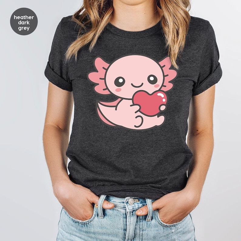 May include: Heather dark grey t-shirt featuring a pink axolotl holding a red heart. The axolotl has large eyes and a small smile.