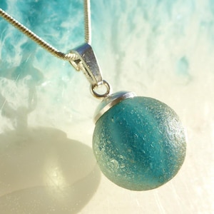 Pendant made of light sea glass ball with light blue inclusions and 925 silver loop