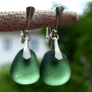 May include: A pair of silver dangle earrings with green sea glass stones. The earrings have a simple, elegant design.