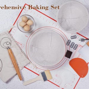 Puede incluir: Un juego de reposter&iacute;a completo con un bol de masa blanco, una esp&aacute;tula de silicona roja, una esp&aacute;tula de masa de madera, una bolsa de lona blanca con un batidor de masa, una estera redonda de lona blanca y tres huevos marrones en un bol transparente.