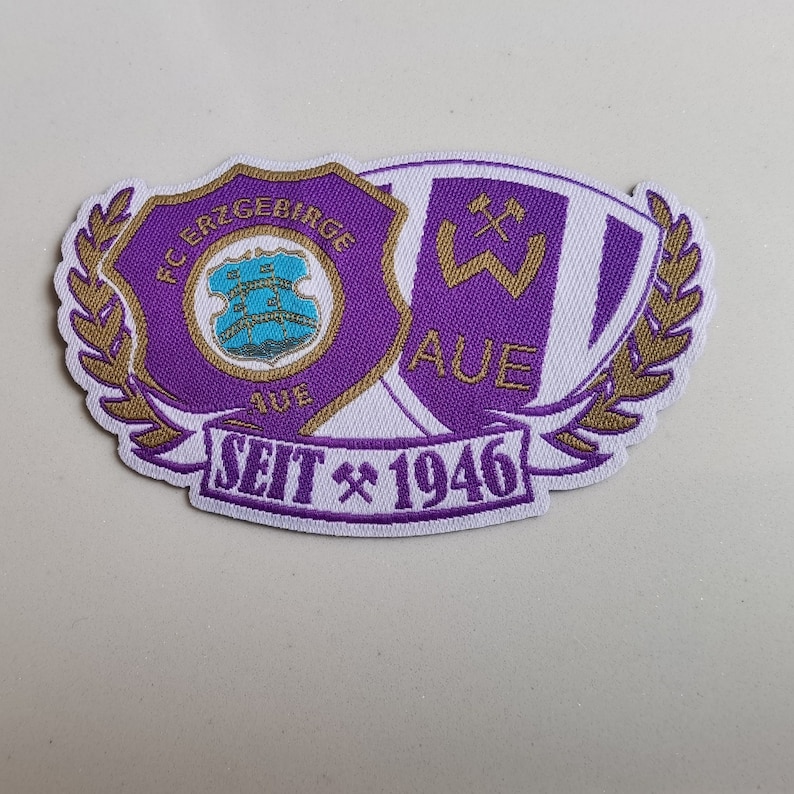 May include: Purple and white embroidered patch with the text "FC Erzgebirge Aue Seit 1946" and a crest with a blue shield and three gold stars.