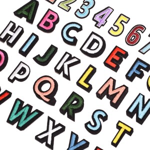 Könnte beinhalten: Ein Set aus bunten Filzbuchstaben und -zahlen. Die Buchstaben sind in verschiedenen Farben, darunter Pink, Blau, Grün, Gelb und Rot. Die Zahlen sind in einem ähnlichen Farbschema gehalten.
