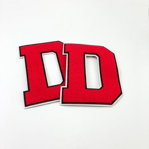 May include: Two red felt letter patches, each with a black outline and a white interior, spelling out the letter "D".
