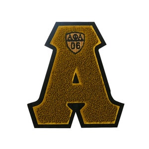 May include: A large, gold felt letter A with a black outline. The letter has a small, gold embroidered shield with the text "APA" and the number "06" inside.