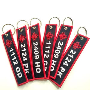 May include: Six black and red keychains with a white maple leaf and white text. The text on the keychains reads "1112 GD", "2124 PK", "2409 HO", "1112 GD", "2409 HO", and "2124 PK".
