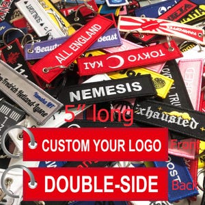 May include: A close-up of a variety of colorful keychains with different designs and text. The keychains are made of fabric and have a 5-inch length. The text on the keychains includes "ALL ENGLAND", "NEMESIS", "TOKYO", "LOVE TRUE", and "CUSTOM YOUR LOGO".