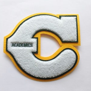 May include: White felt letter C with a green outline and a yellow outline. The letter is surrounded by a yellow border. The word "ACADEMICS" is embroidered in green on the letter.