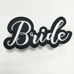 Puede incluir: Parche de fieltro negro con el texto "Bride" bordado en blanco.
