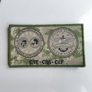 May include: A green and tan camouflage patch with the text "U.S. NAVAL FORCES EUROPE", "US. NAVAL FORCES AFRICA", "UNITED STATES", "SIXTH FLEET", and "CNE-CNA-C6F".